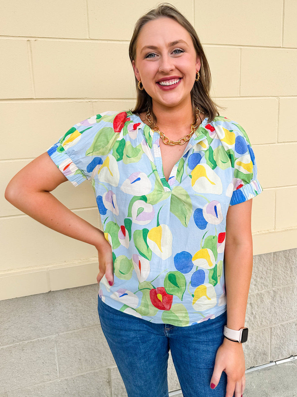  Light blue floral top with a split neckline and elastic short sleeves, featuring a bright, colorful print—styled for spring or summer wear.
