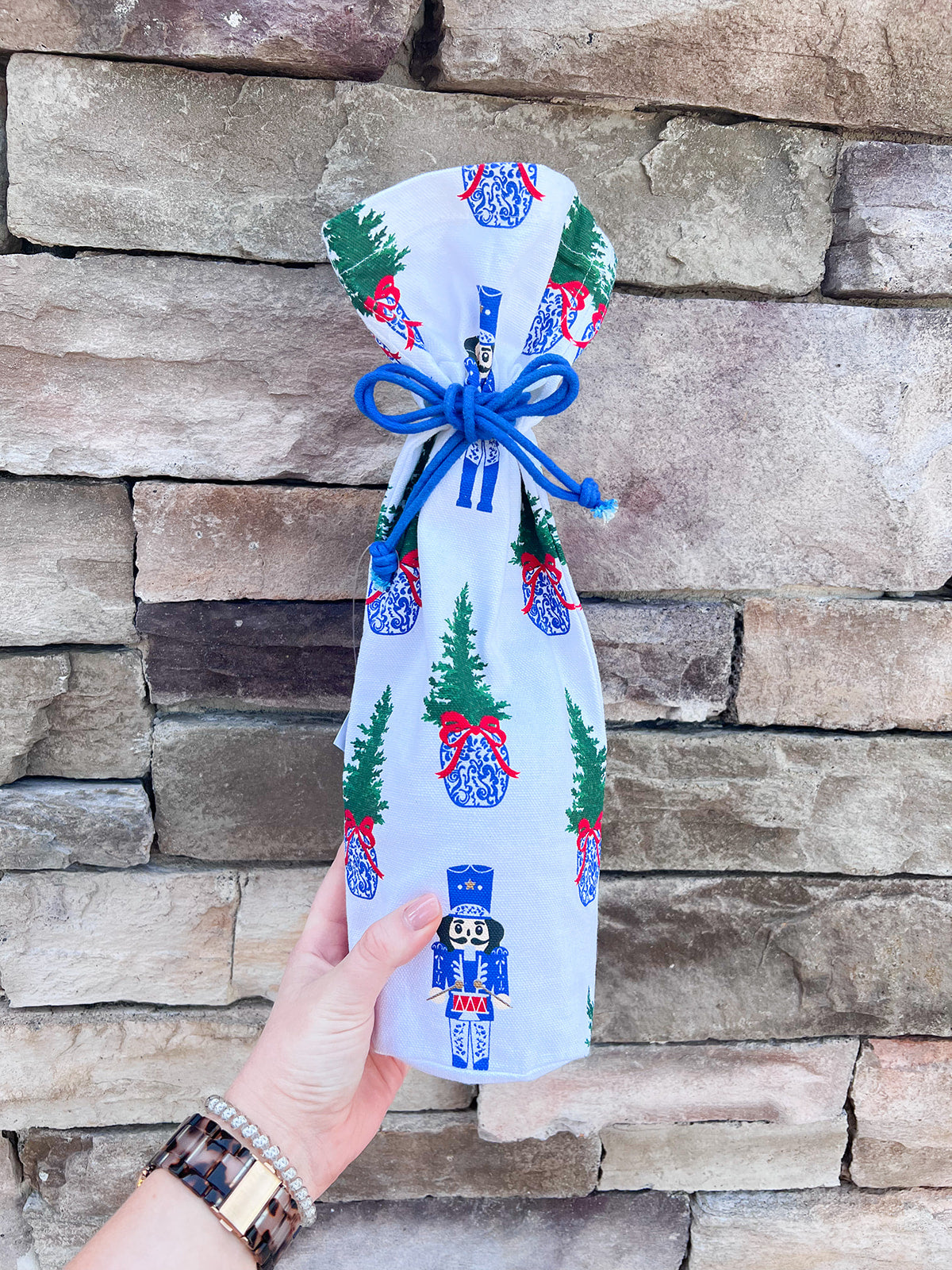 White bottle pouch with nutcracker and Christmas tree print, blue drawstring closure.