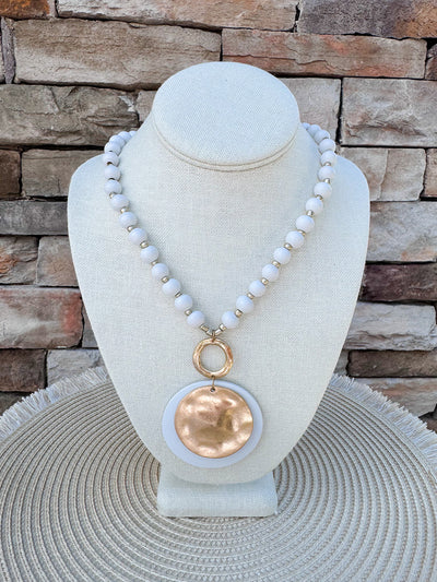 Cream beaded necklace with gold accents and a layered hammered gold and cream pendant, styled for versatile wear.