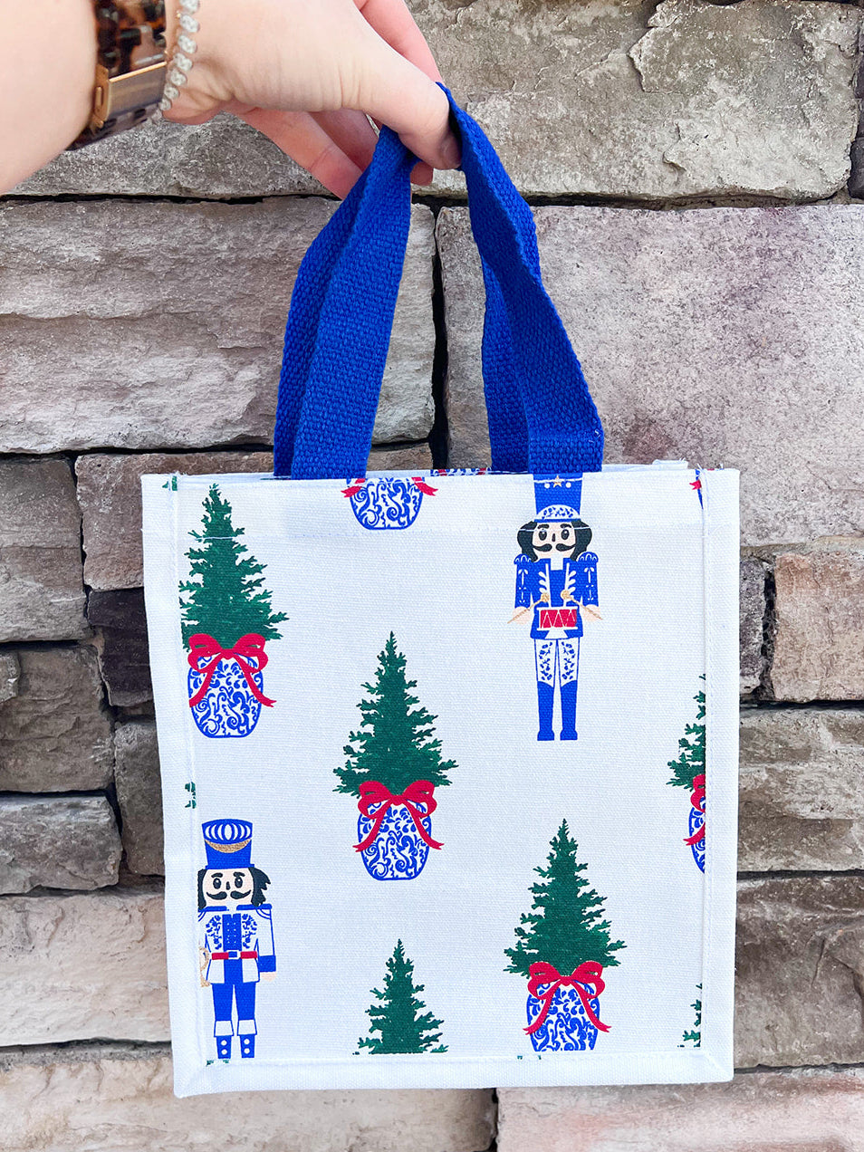 White compact tote with nutcracker and tree print and blue handles.