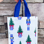White compact tote with nutcracker and tree print and blue handles.