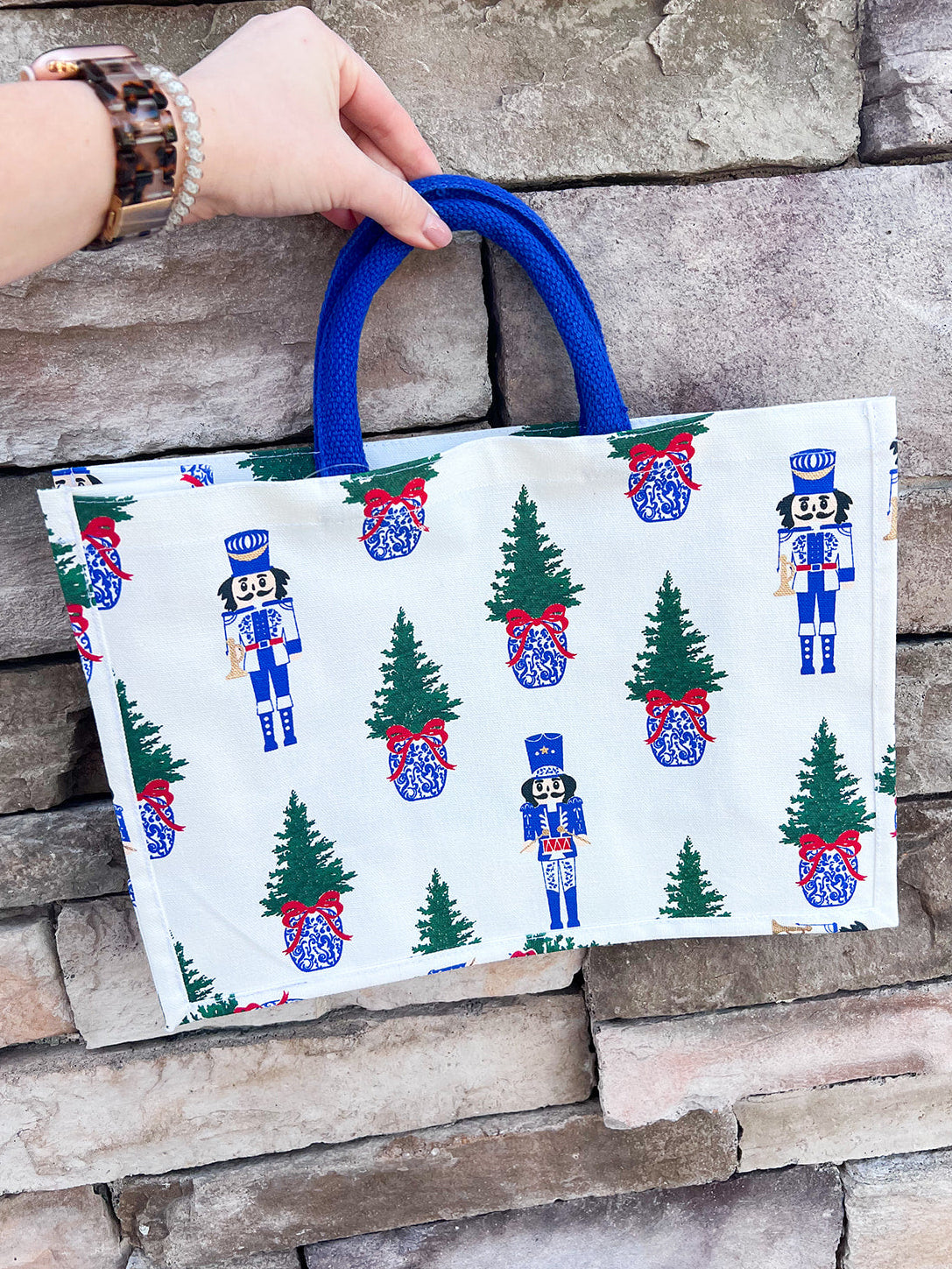 White rectangular market tote with nutcracker print and blue handles.