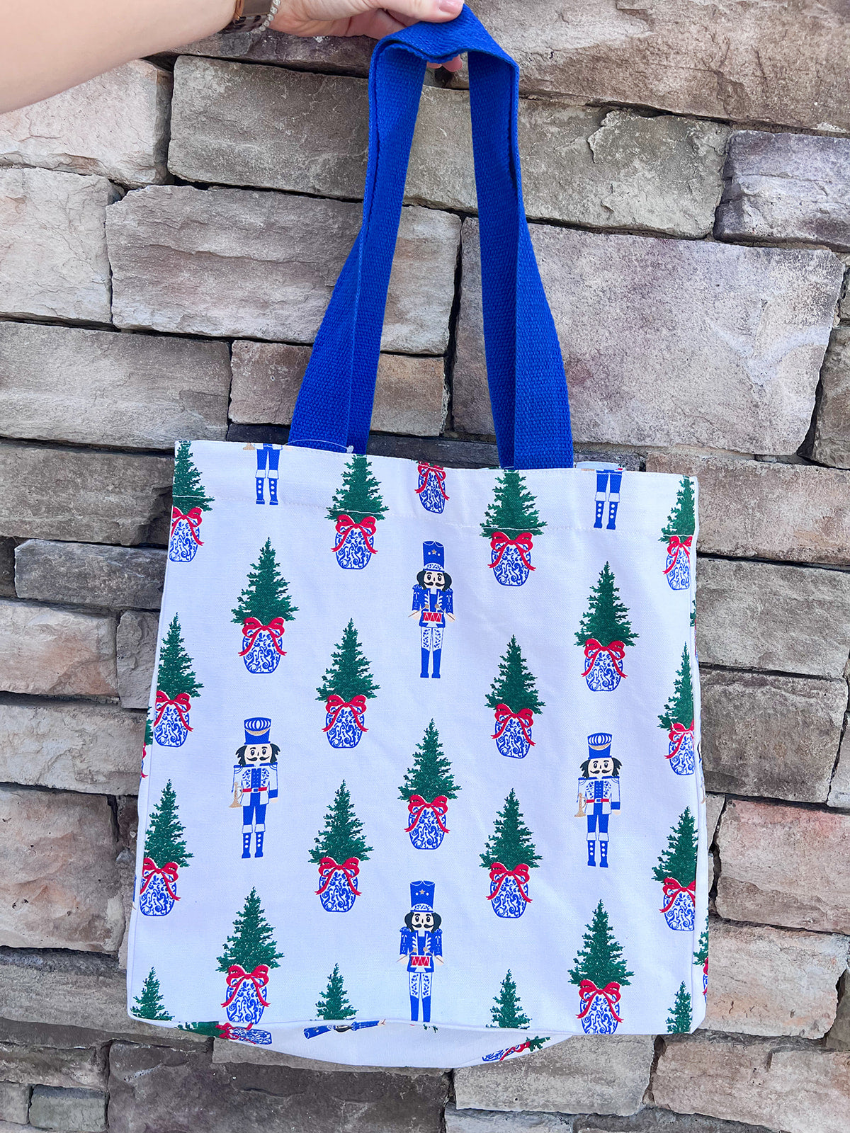 White everyday tote with nutcracker and Christmas tree print and blue handles.