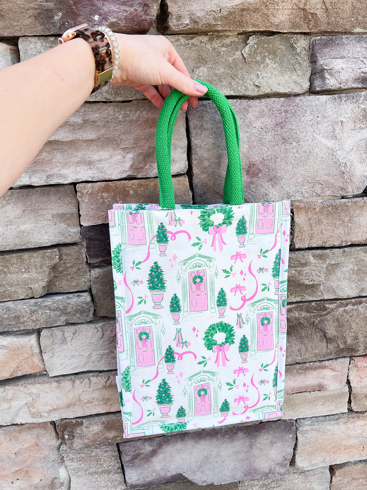 Tote bag with pink and green design held against a stone wall