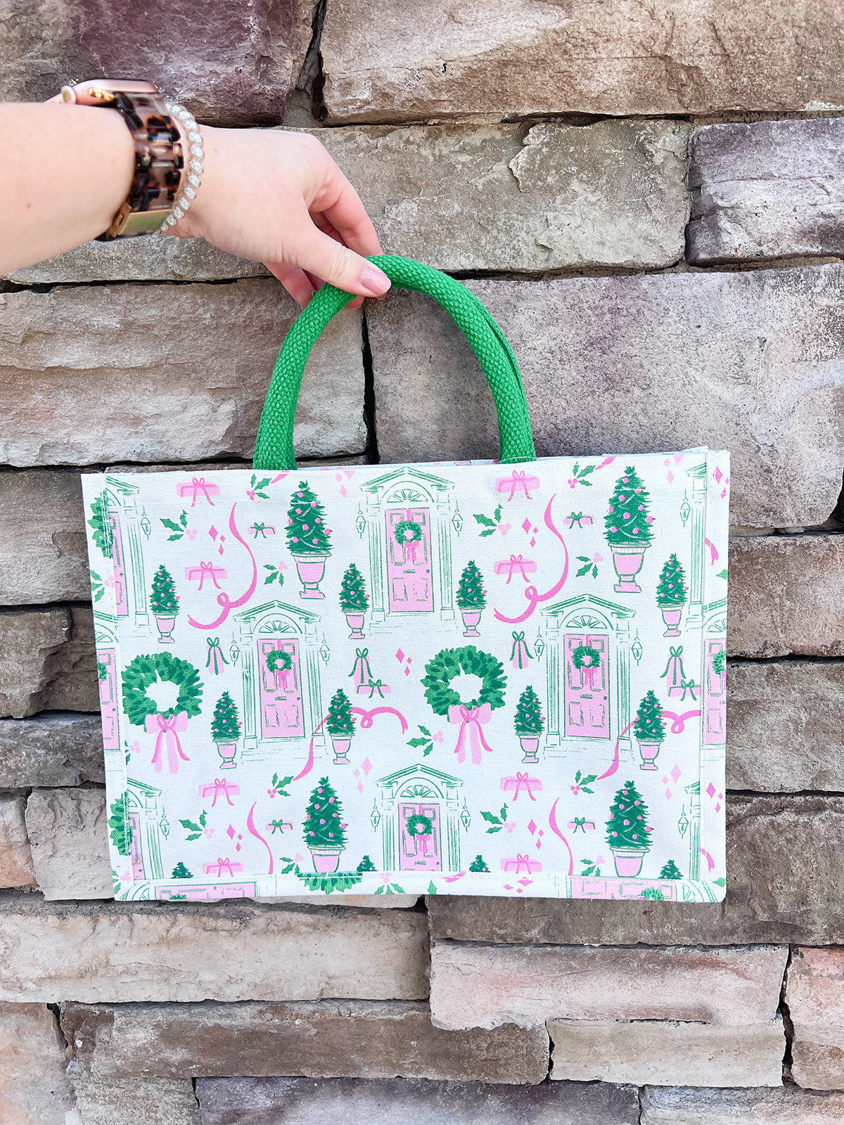 White rectangular market tote with pink and green holiday print featuring front doors, wreaths, potted trees, and green handles.