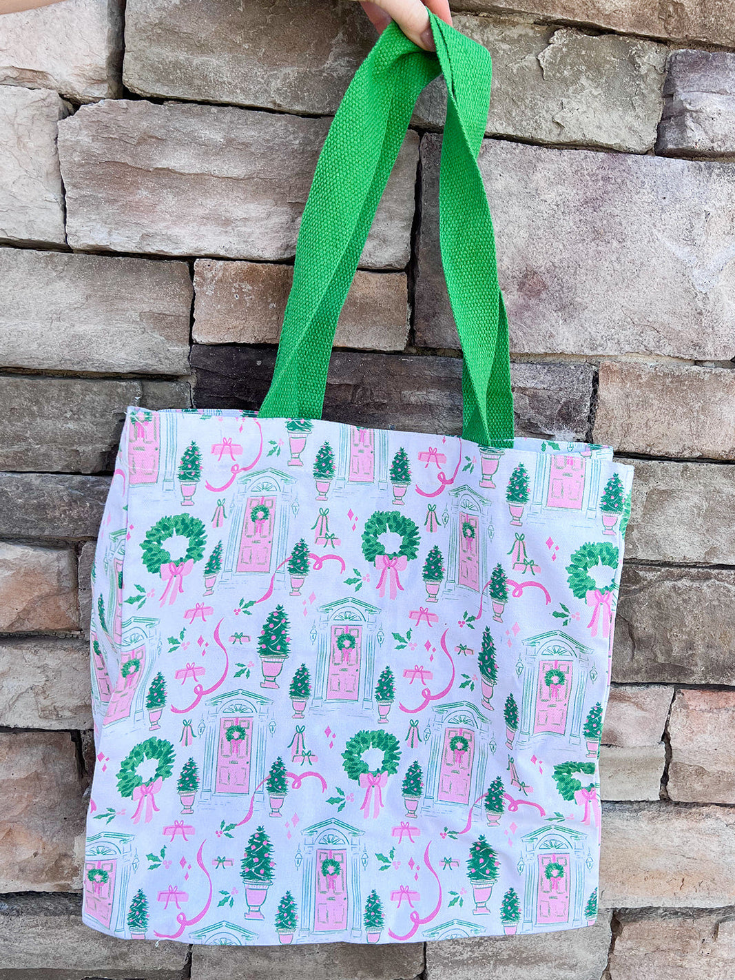 Tote bag with festive design featuring pink doors, green wreaths, and ribbons on a white background.