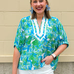 White caftan top with green and blue abstract floral print, split neckline, and dolman sleeves with elastic cuffs—lightweight and flowy