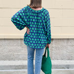 Flowy navy and green patterned blouse with tie-neck, ruffle collar, dolman sleeves, and elastic cuffs—lightweight and oversized