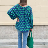 Flowy navy and green patterned blouse with tie-neck, ruffle collar, dolman sleeves, and elastic cuffs—lightweight and oversized