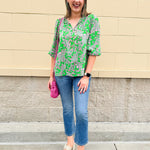 Green and pink paisley print blouse with frilled tie neckline and three-quarter peasant sleeves displayed on hanger against a neutral background