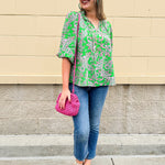 Green and pink paisley print blouse with frilled tie neckline and three-quarter peasant sleeves displayed on hanger against a neutral background