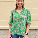 Green and pink paisley print blouse with frilled tie neckline and three-quarter peasant sleeves displayed on hanger against a neutral background