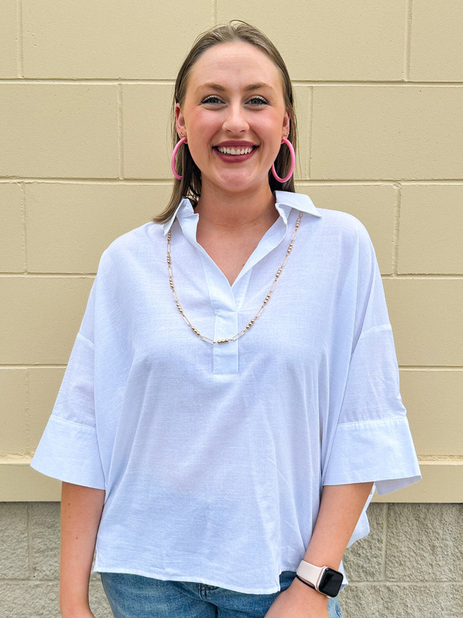 Oversized off-white V-neck popover shirt with collar and cuffed sleeves, styled casually for warm weather.