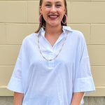 Oversized off-white V-neck popover shirt with collar and cuffed sleeves, styled casually for warm weather.