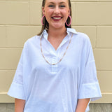 Oversized off-white V-neck popover shirt with collar and cuffed sleeves, styled casually for warm weather.
