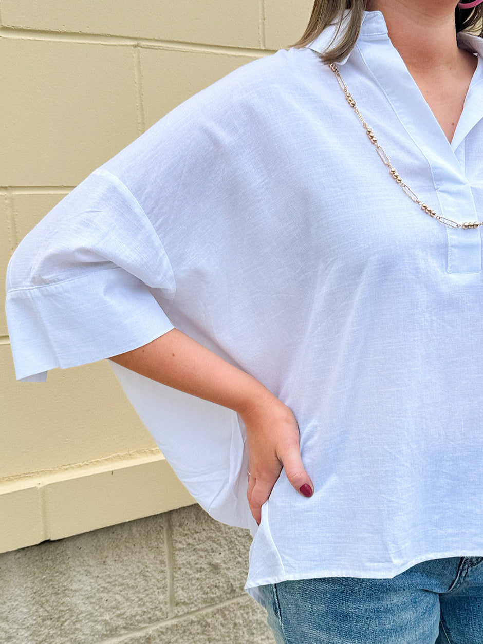 Oversized off-white V-neck popover shirt with collar and cuffed sleeves, styled casually for warm weather.