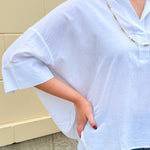 Oversized off-white V-neck popover shirt with collar and cuffed sleeves, styled casually for warm weather.