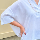 Oversized off-white V-neck popover shirt with collar and cuffed sleeves, styled casually for warm weather.