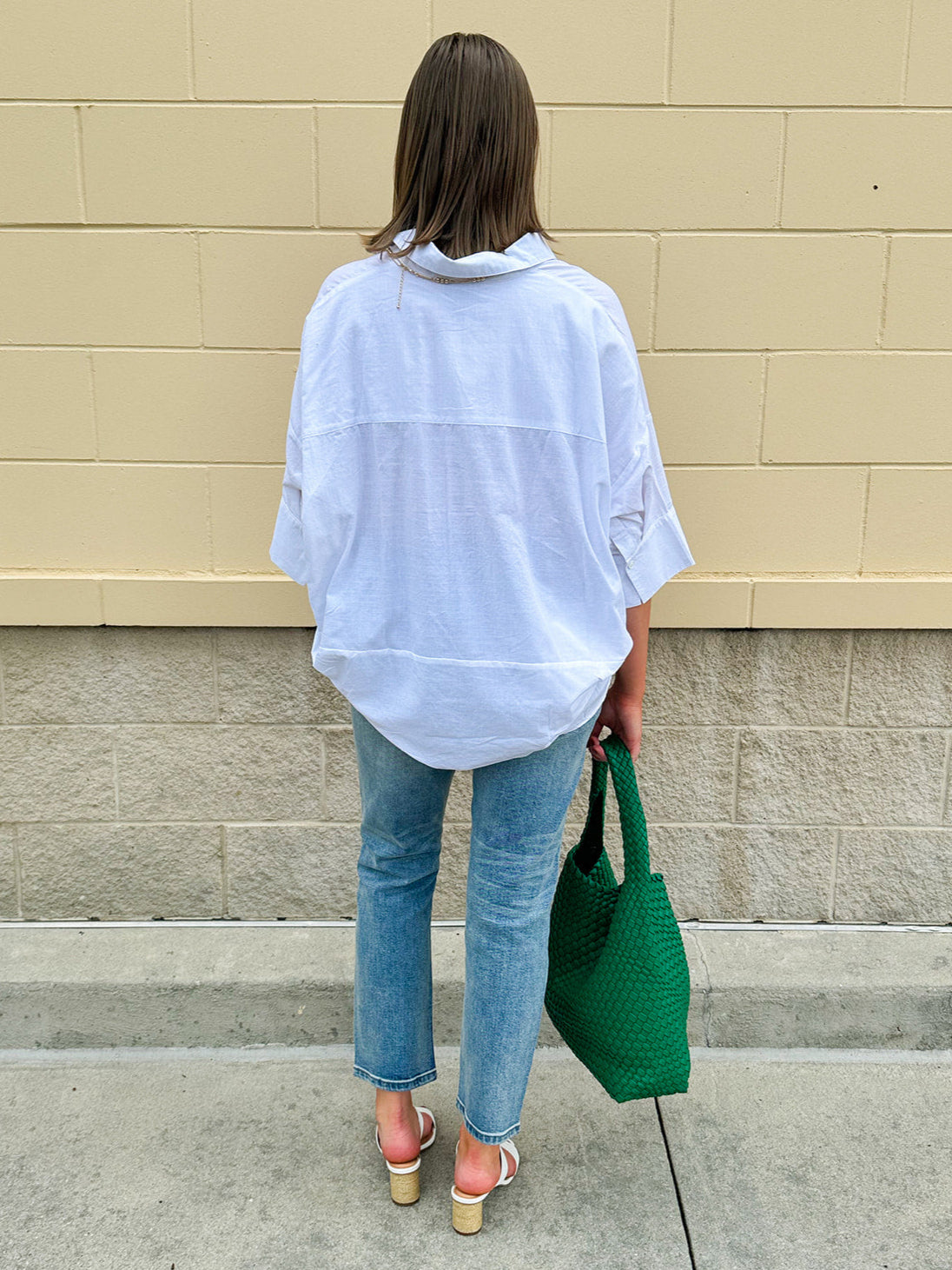 Oversized off-white V-neck popover shirt with collar and cuffed sleeves, styled casually for warm weather.