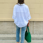 Oversized off-white V-neck popover shirt with collar and cuffed sleeves, styled casually for warm weather.