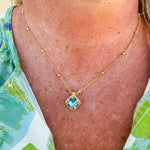 Bright gold-tone necklace featuring a square-cut aquamarine crystal with metal beaded halo on an adjustable chain.