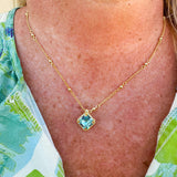 Bright gold-tone necklace featuring a square-cut aquamarine crystal with metal beaded halo on an adjustable chain.