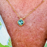 Bright gold-tone necklace featuring a square-cut aquamarine crystal with metal beaded halo on an adjustable chain.
