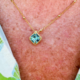 Bright gold-tone necklace featuring a square-cut aquamarine crystal with metal beaded halo on an adjustable chain.