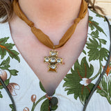 Bronze scarf-style necklace with knotted details and gold cross pendant accented with gemstones.