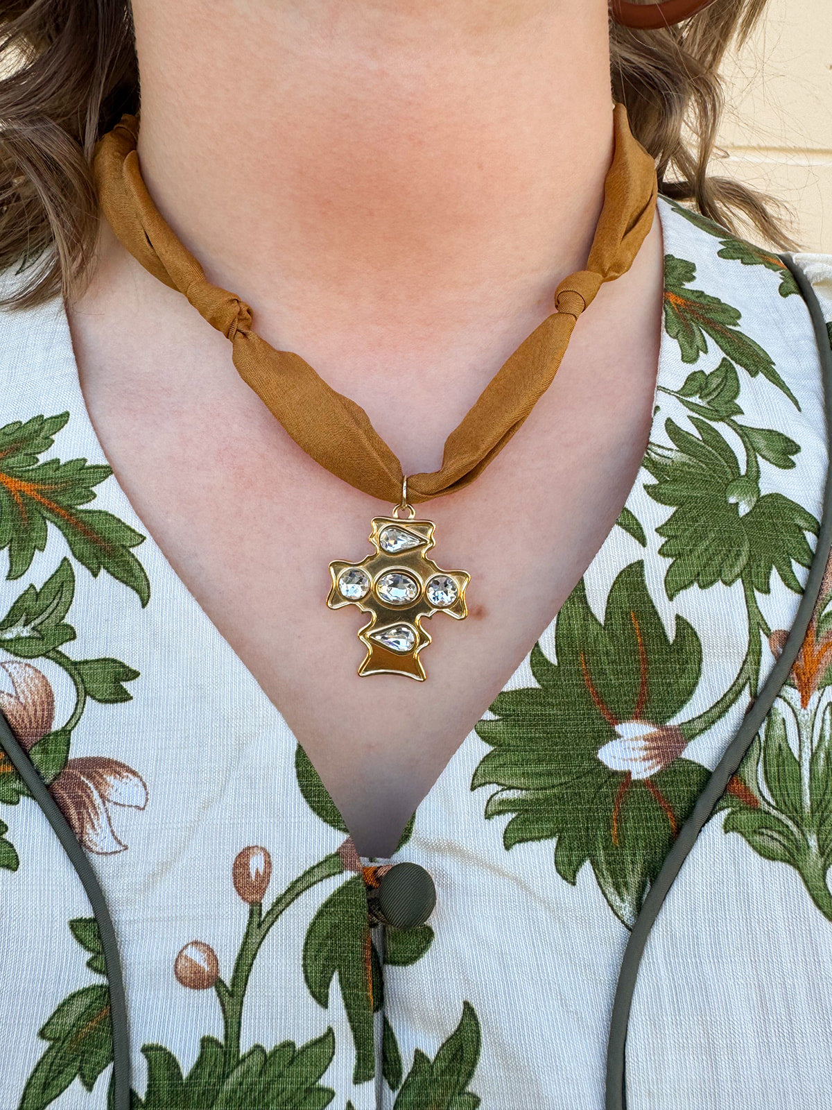 Bronze scarf-style necklace with knotted details and gold cross pendant accented with gemstones.