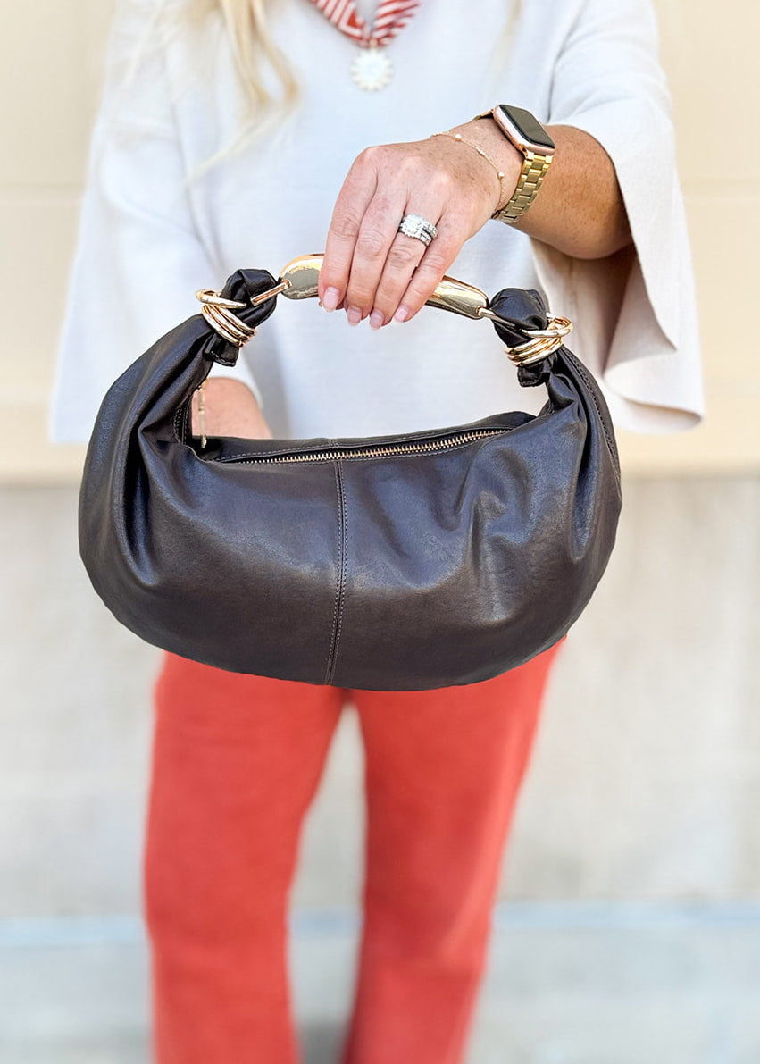 Chocolate brown asymmetrical pleather handbag with gold handle, gold hardware, and detachable crossbody strap.