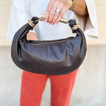 Chocolate brown asymmetrical pleather handbag with gold handle, gold hardware, and detachable crossbody strap.