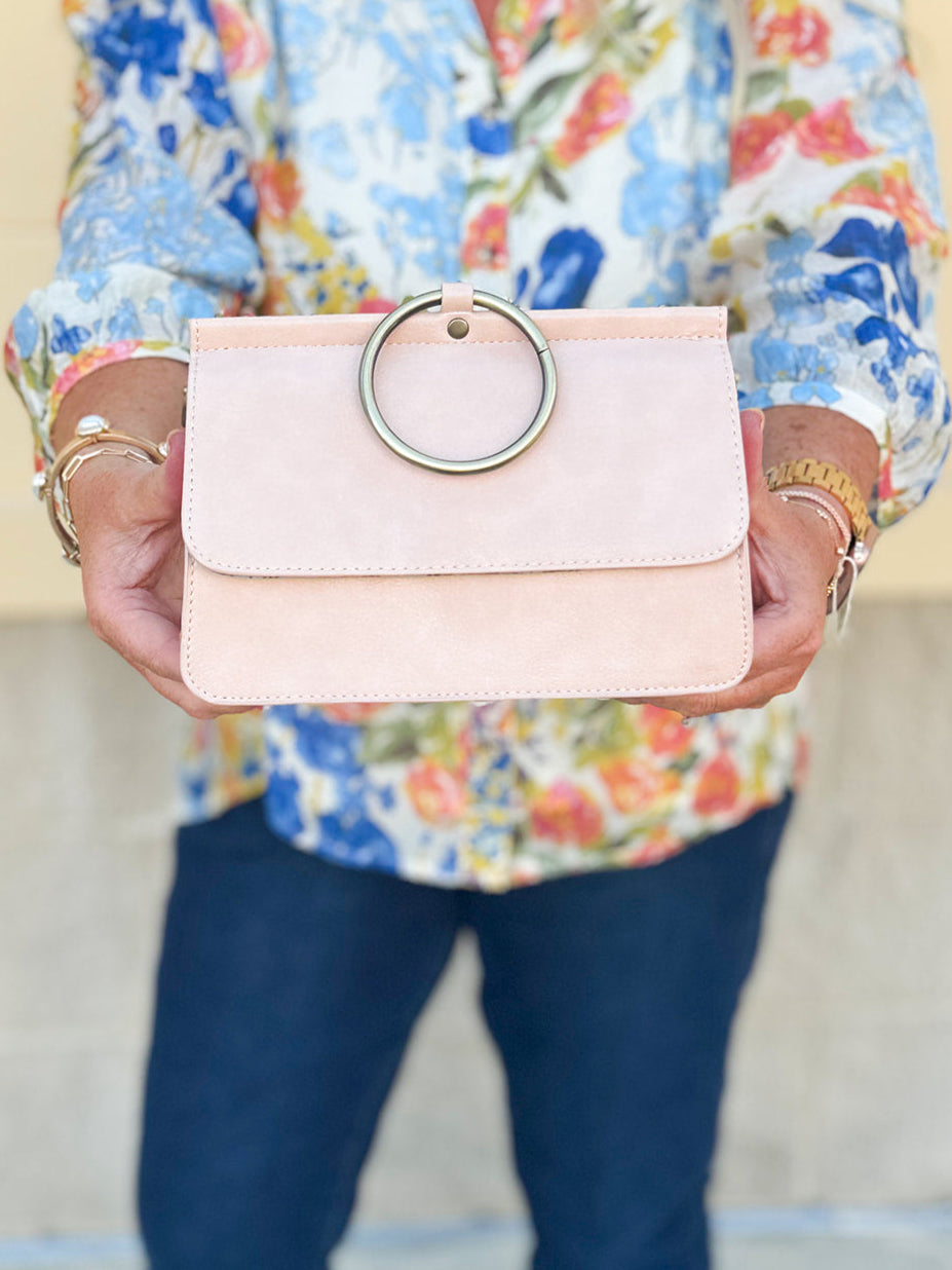 Soft pink structured handbag with gold ring handle and optional crossbody strap.