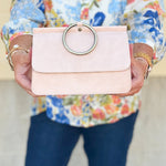 Soft pink structured handbag with gold ring handle and optional crossbody strap.