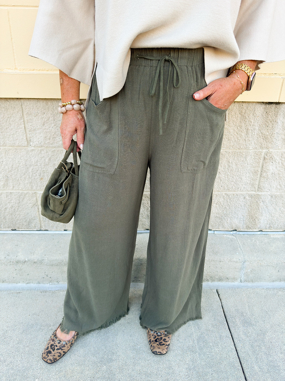 Olive wide-leg linen pants with drawstring waist, cropped length, and frayed hem.