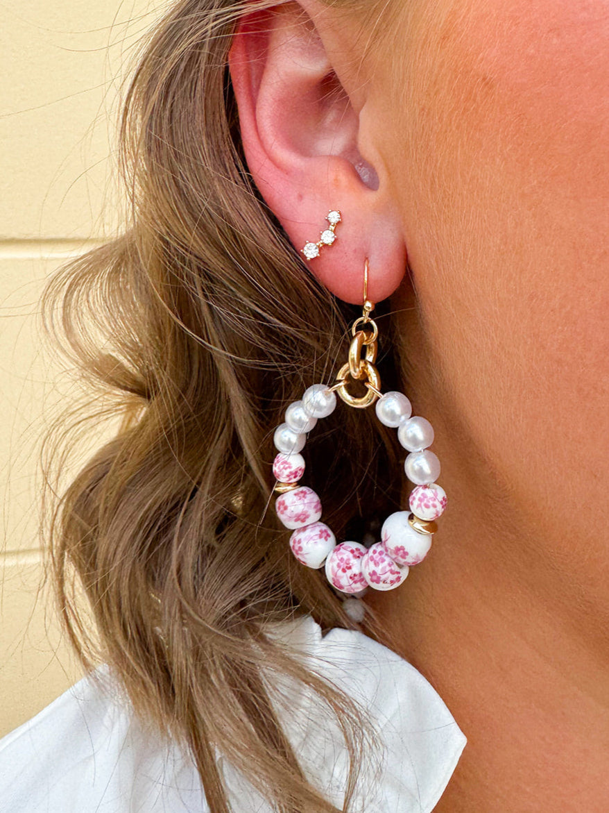 A pair of floral ceramic hoop earrings with pink, featuring hand-painted ceramic beads, glass pearls, and gold-tone accents.