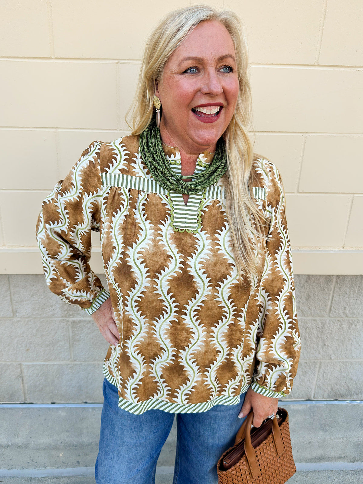 Printed V-neck long sleeve blouse with brown, cream, and olive tones, contrasting stripe accents, and decorative trim.
