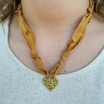 Gold scarf-style necklace with knotted details and hammered metal heart pendant.