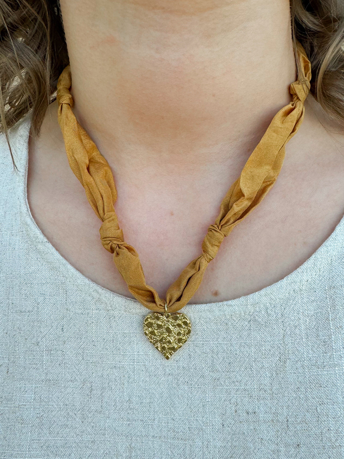 Gold scarf-style necklace with knotted details and hammered metal heart pendant.