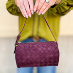 Plum-colored cylinder-shaped shoulder bag with adjustable buckle strap and zip closure.