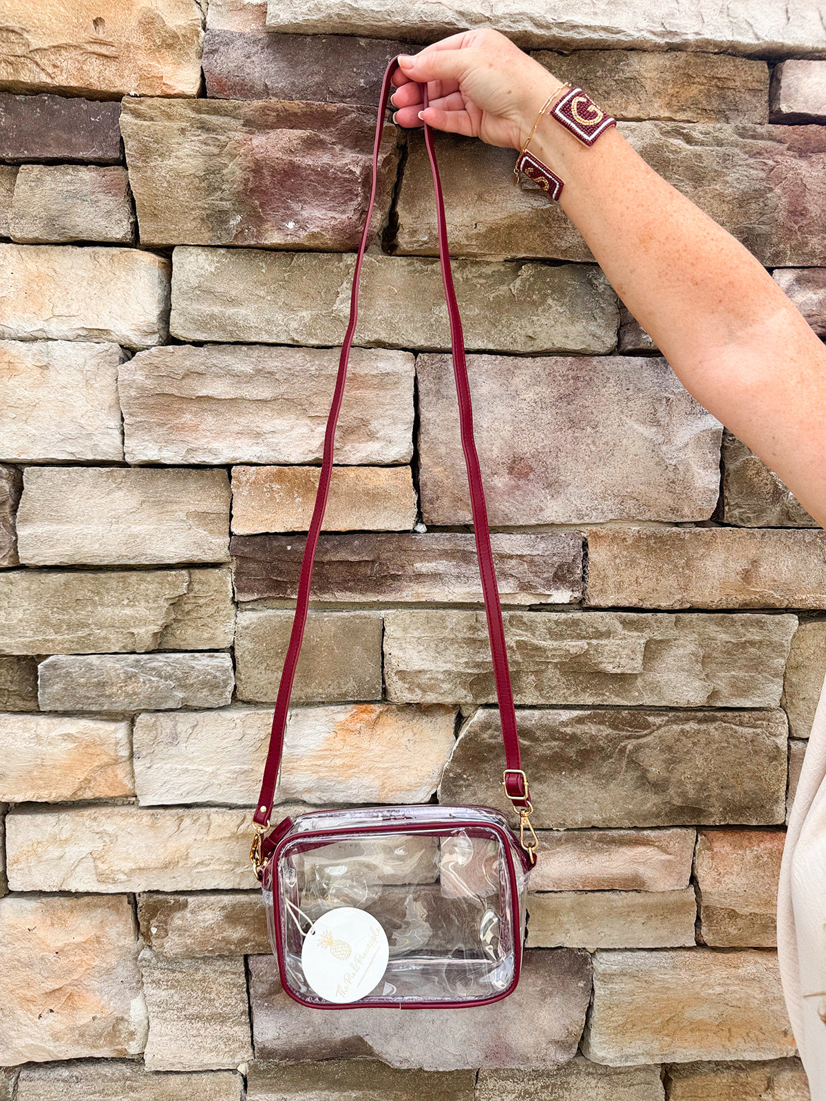 Clear crossbody purse with garnet vegan leather trim and brass hardware, designed for stadium approval and gameday style.