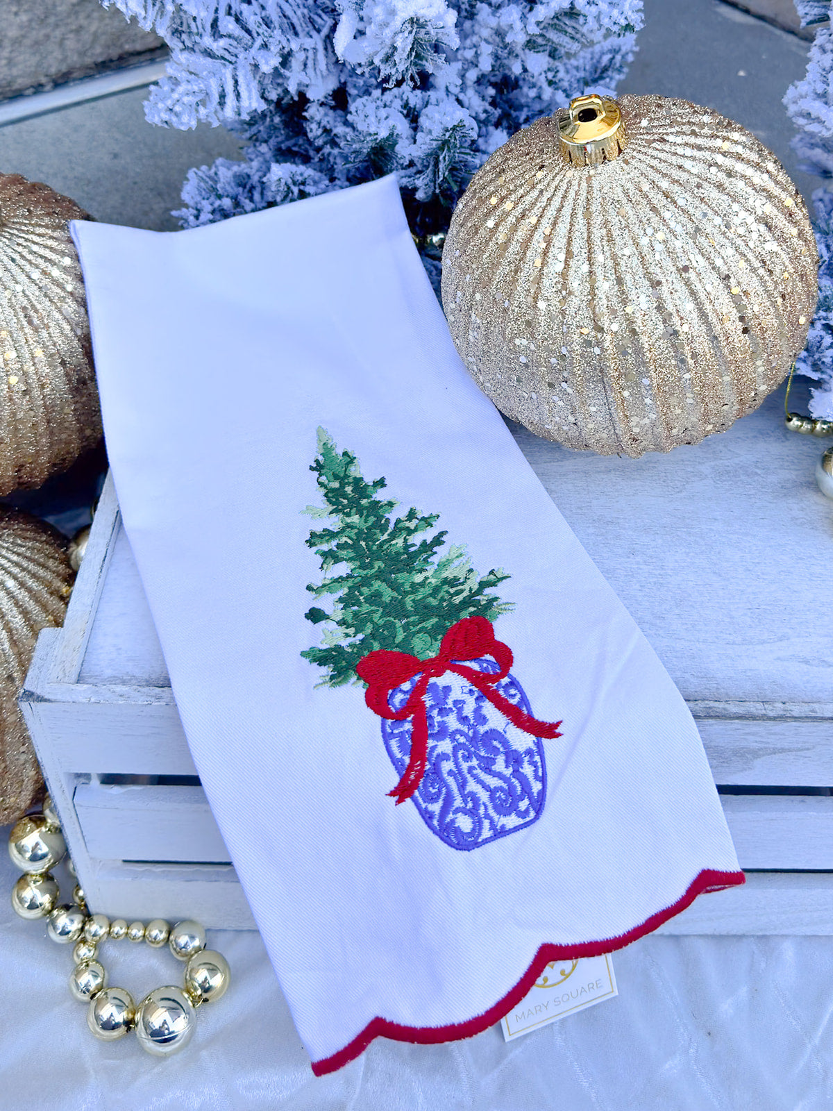 White tea towel with blue and white ginger jar Christmas tree, red bow, and red scalloped trim.