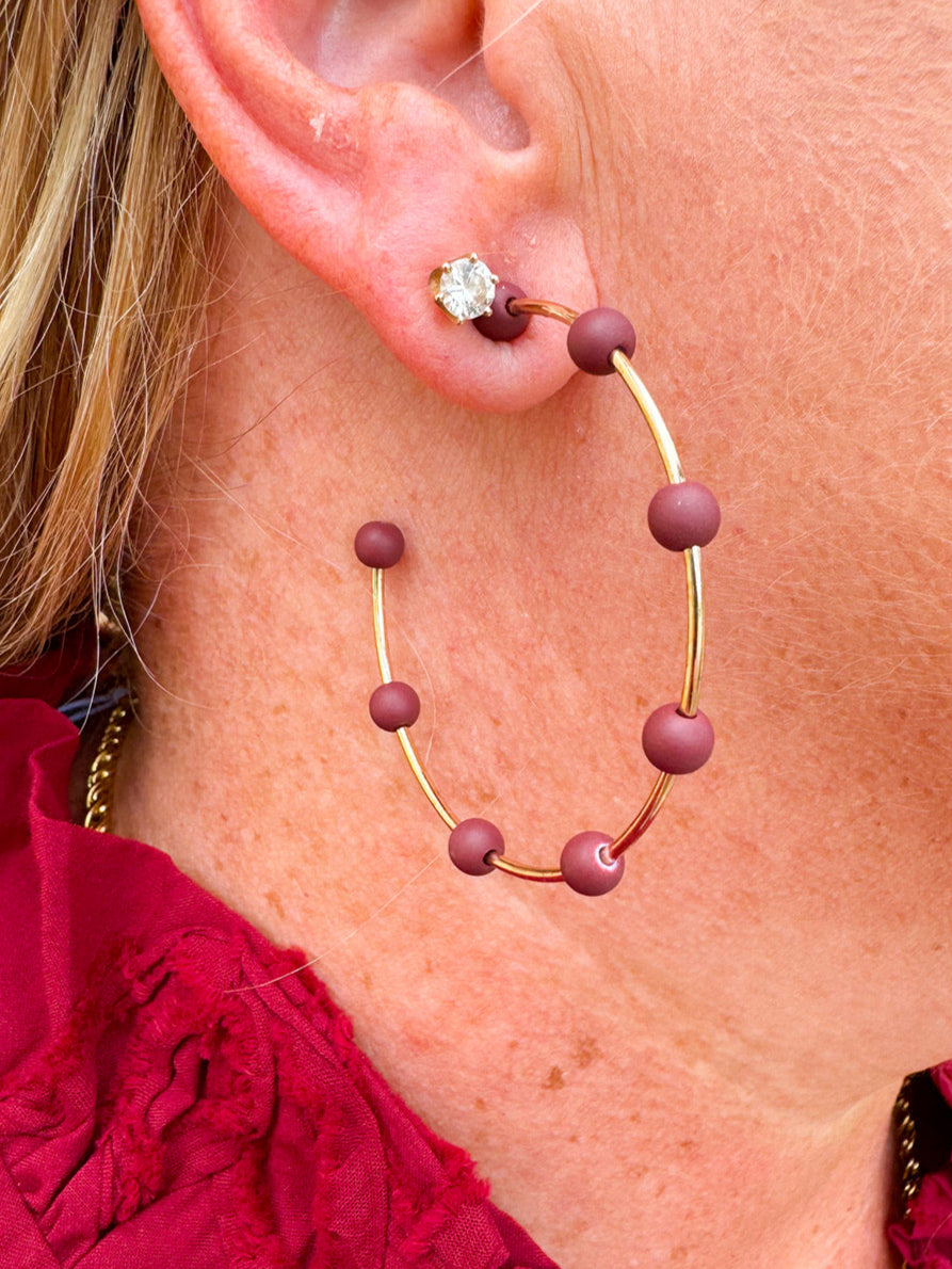 Gold hoop earrings with maroon-coated metal bead accents, offering a bold yet elegant pop of color.