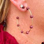 Gold hoop earrings with maroon-coated metal bead accents, offering a bold yet elegant pop of color.