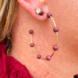 Gold hoop earrings with maroon-coated metal bead accents, offering a bold yet elegant pop of color.
