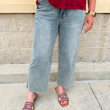 Model wearing light wash, cropped wide leg jeans with raw hem and light distressing. Jeans feature a mid-rise waist and tummy control panel.