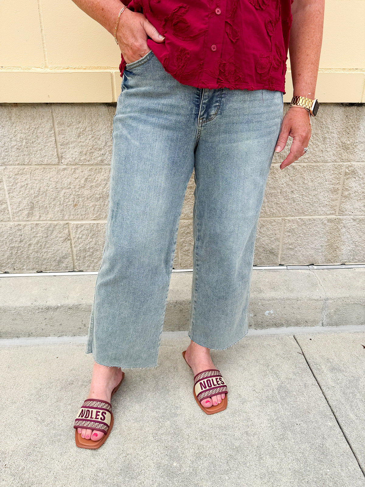 Model wearing light wash, cropped wide leg jeans with raw hem and light distressing. Jeans feature a mid-rise waist and tummy control panel.
