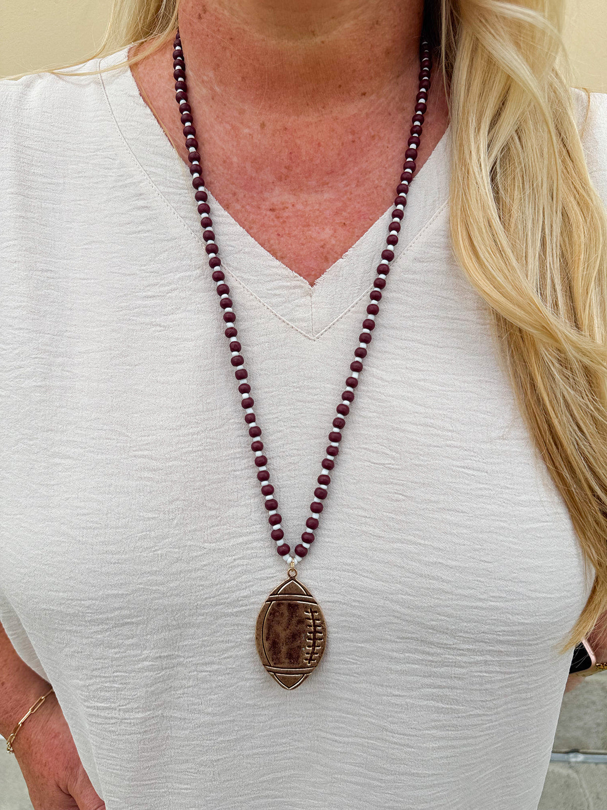 Long beaded necklace with alternating garnet and white beads, featuring a gold football pendant. A bold yet fun Gameday accessory.
