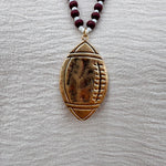 Long beaded necklace with alternating garnet and white beads, featuring a gold football pendant. A bold yet fun Gameday accessory.