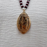 Long beaded necklace with alternating garnet and white beads, featuring a gold football pendant. A bold yet fun Gameday accessory.